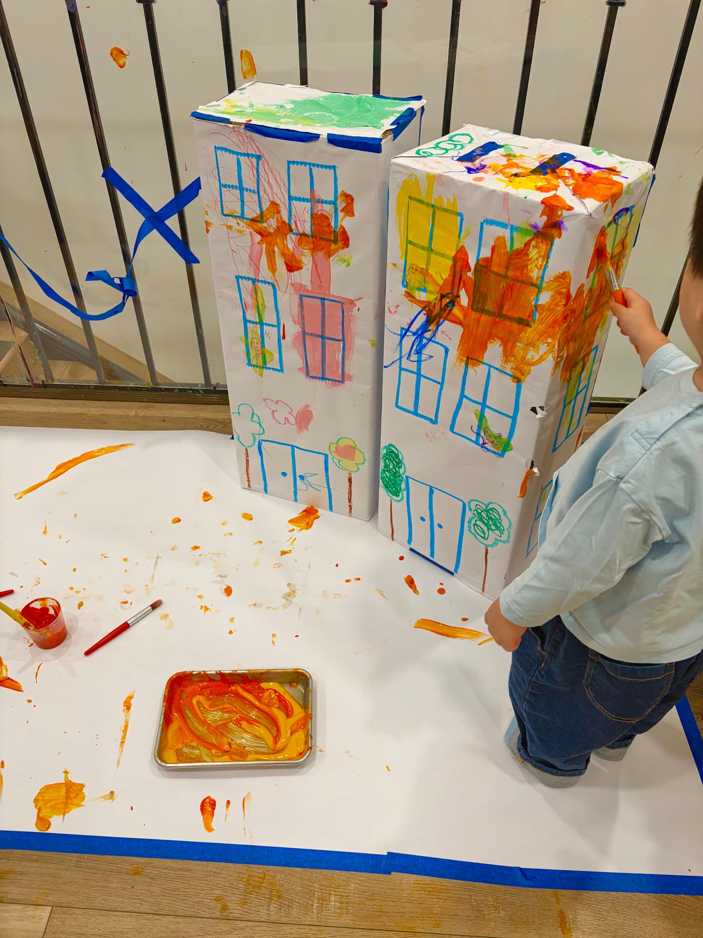 Child with green paint-covered hands in a blue smock