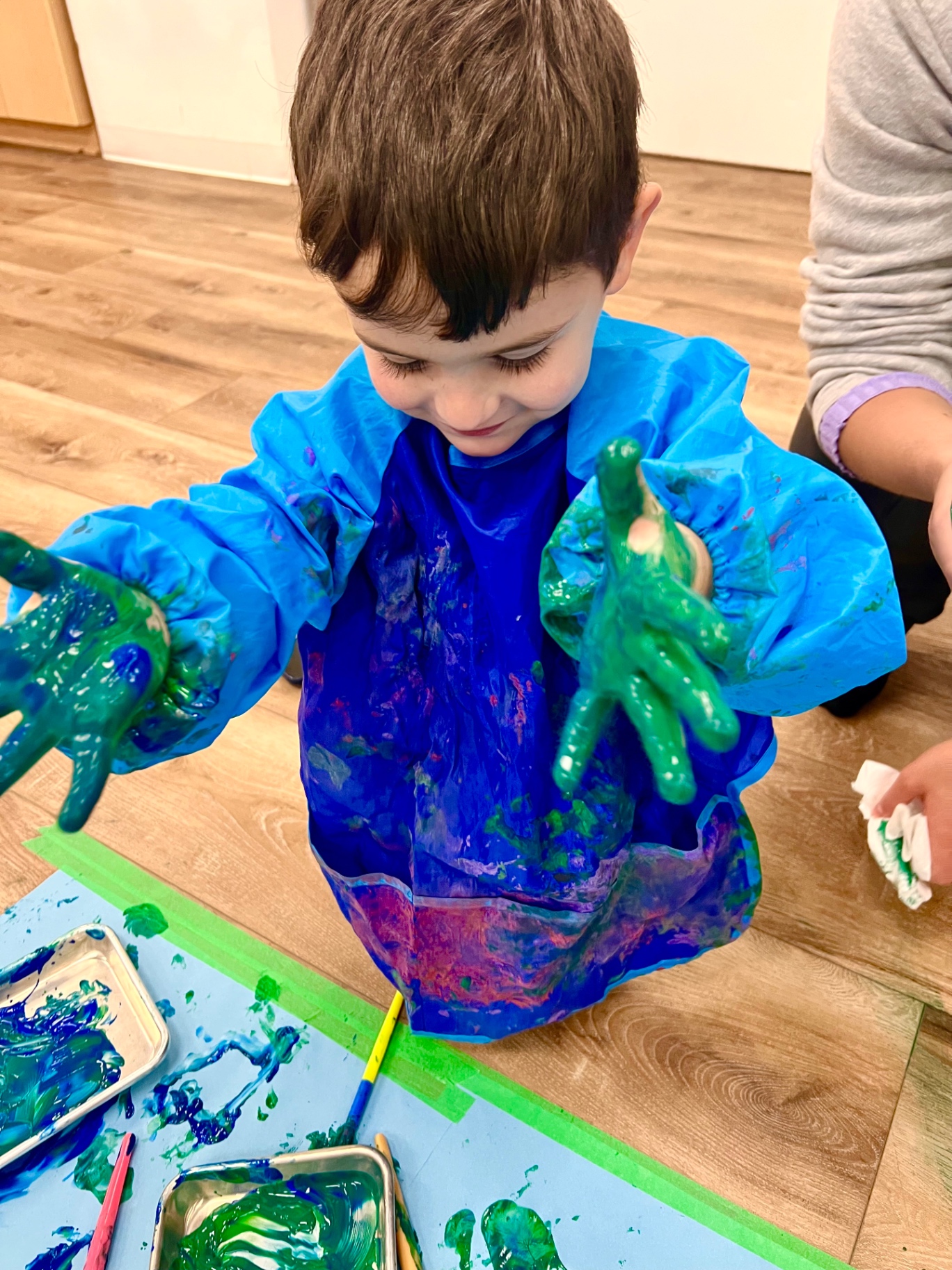 Child with green paint-covered hands in a blue smock