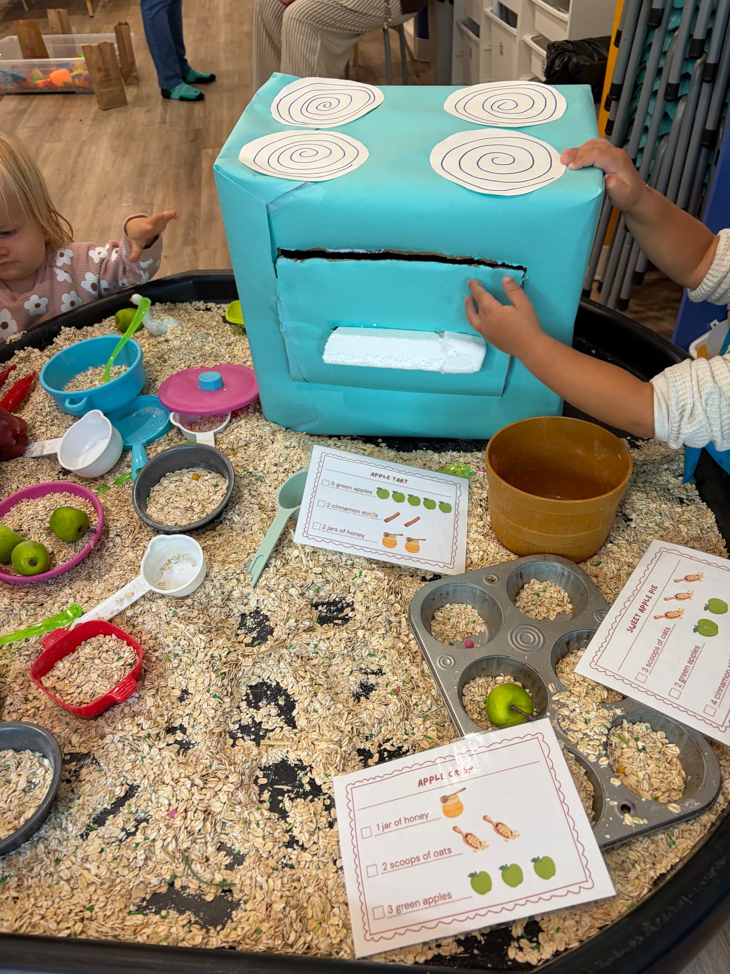 Toddlers exploring a rainbow tape and pom-pom wall